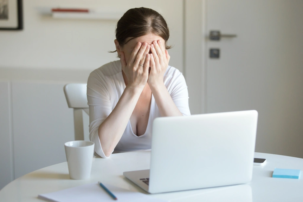portrait-woman-desk-with-laptop-hands-closing-face_1.webp